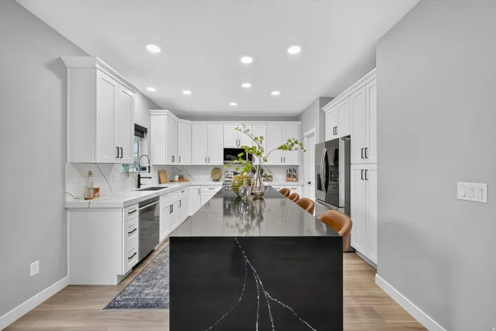 Kitchen featuring a large dark stone island with light veining, white shaker-style cabinetry, and light wood-finish flooring