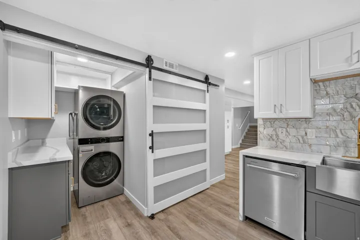 Laundry area featuring a stacked washer and dryer, barn door, and wood-finish flooring