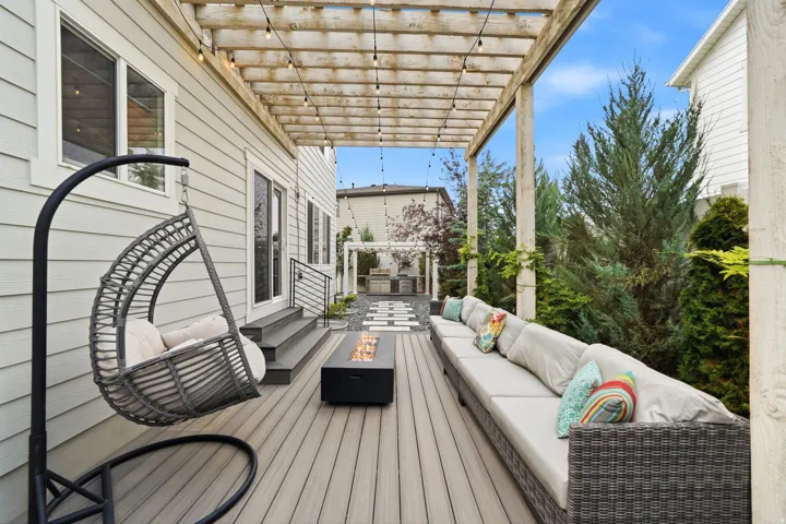 Expansive outdoor deck featuring a composite wood-finish surface, a wooden pergola with string lighting, a gas fire pit, and substantial landscaping