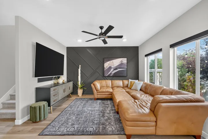 Living area featuring wood-finish flooring, a contemporary accent wall with geometric paneling, and a ceiling fan with integrated lighting
