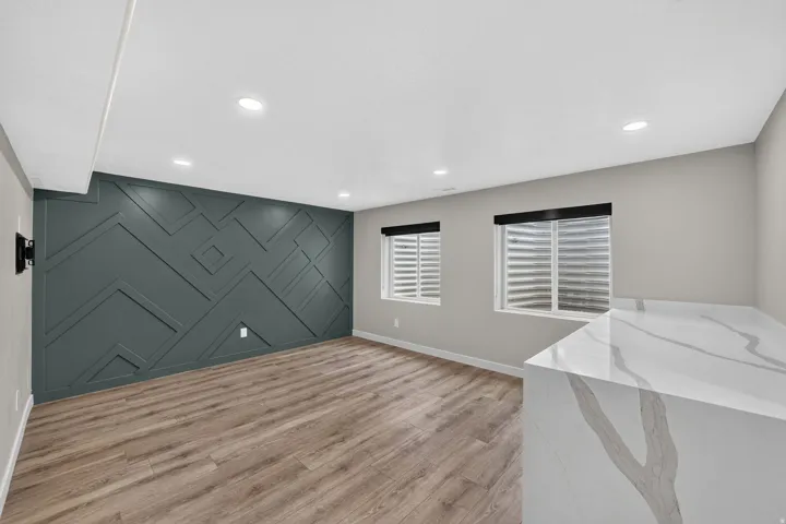 Recreation room featuring a decorative accent wall, recessed lighting, wood-finish flooring, two windows with blinds, and a waterfall-edge countertop