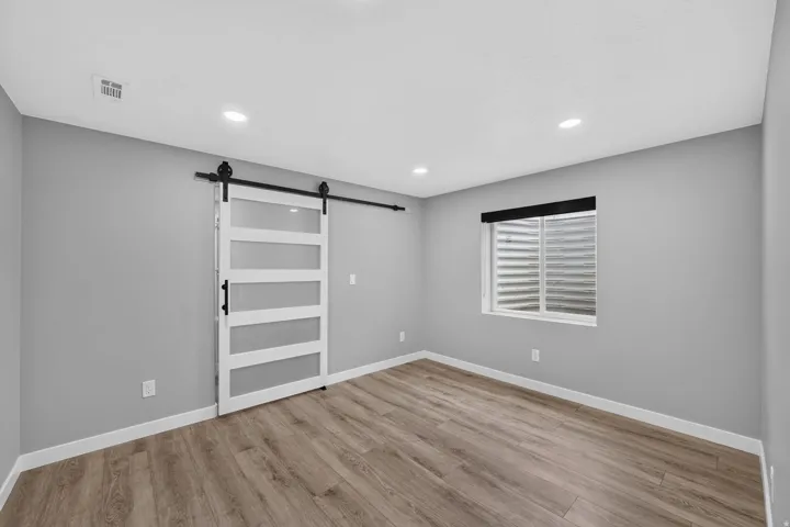 Versatile room featuring a modern barn door with frosted glass panels, recessed lighting, and wood-finish flooring