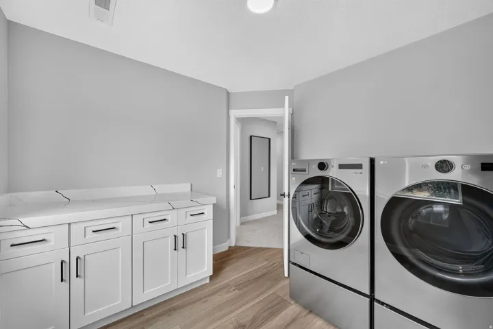 Laundry area featuring light wood-finish flooring, white cabinetry with dark hardware, and a white countertop with a partial backsplash