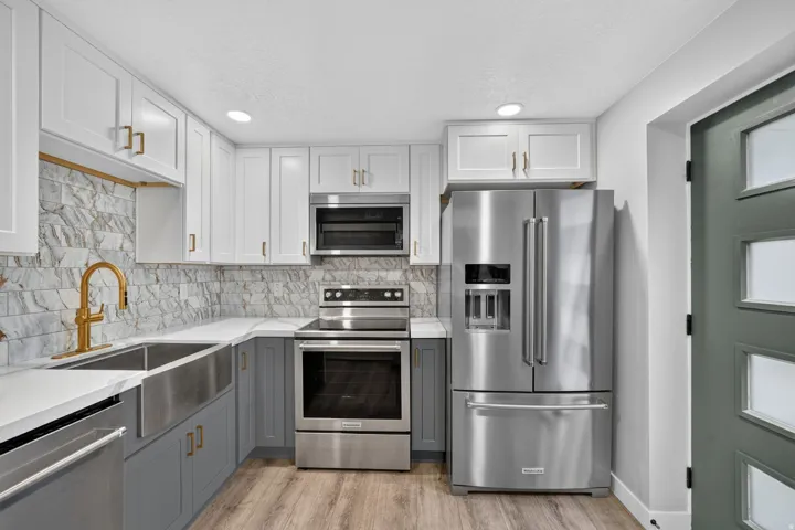 Kitchen featuring two-tone cabinetry with gold-tone hardware, stainless steel appliances, a farmhouse-style sink with a gold-tone faucet, and stone-look tile backsplash