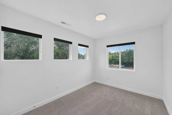 Bright room featuring four windows with black roller shades, white walls, and gray carpet flooring