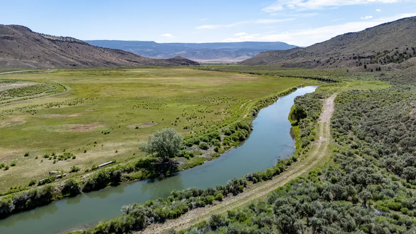 Expanse of open land featuring a river, natural foliage, and distant mountains under a clear sky