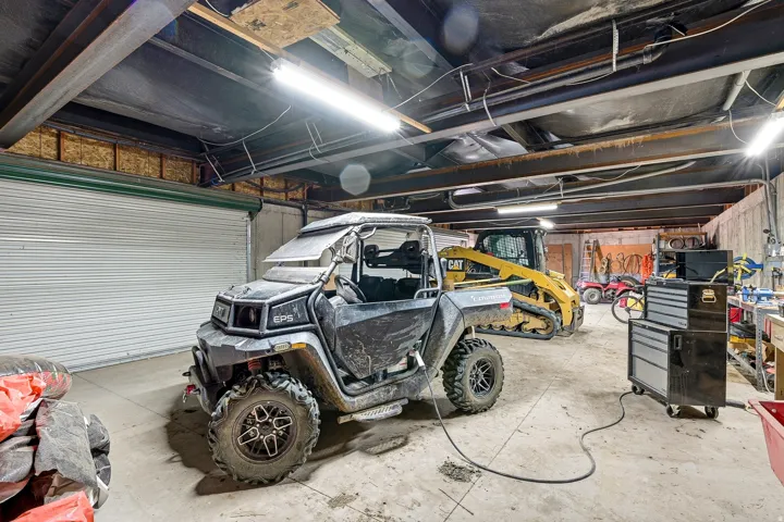 Spacious utility building featuring a concrete floor, exposed beam ceiling, steel roll-up door, and fluorescent lighting fixtures