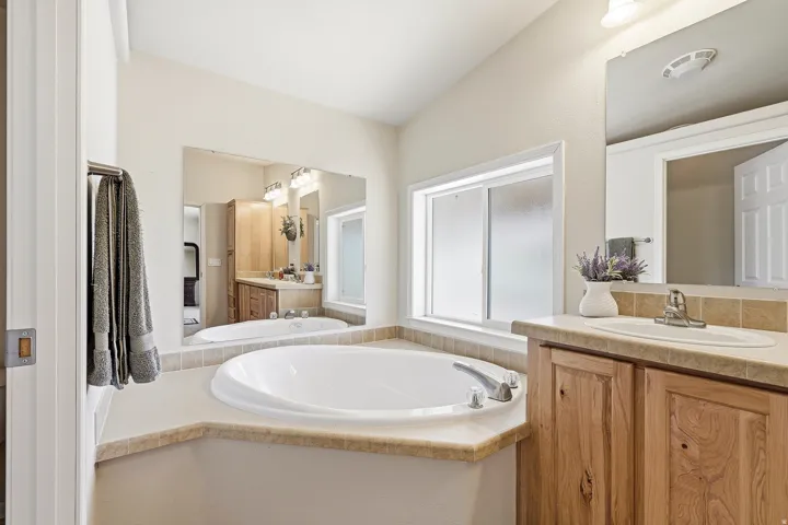 Bathroom featuring a built-in soaking tub, a window with frosted glass, a single vanity with wood-finish cabinetry, a white basin sink, and a large wall-mounted mirror