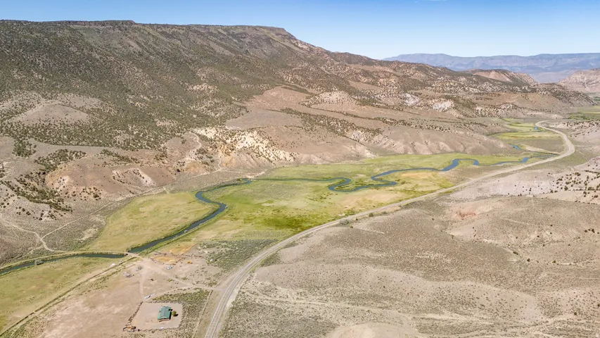 Sweeping aerial perspective showcasing a river meandering through a verdant valley with a single-story residence and a paved road