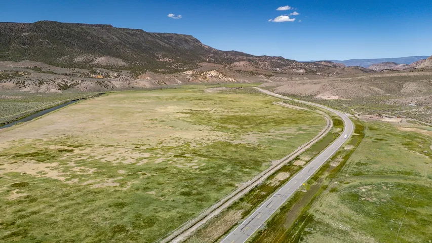 Expansive open land featuring natural grasses, a winding river, and a paved road, all set against a mountainous backdrop