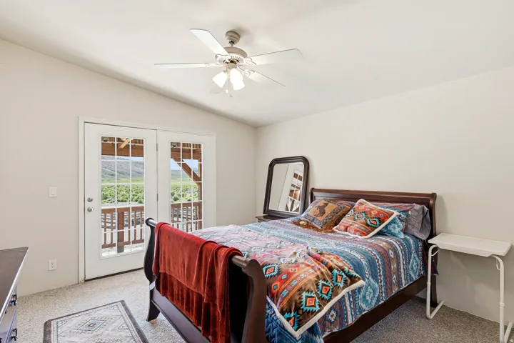 Carpeted room featuring a vaulted ceiling with a ceiling fan, light-colored walls, and French doors opening to an exterior deck