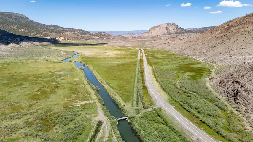 Expansive valley landscape featuring a river, verdant grasslands, and a paved road