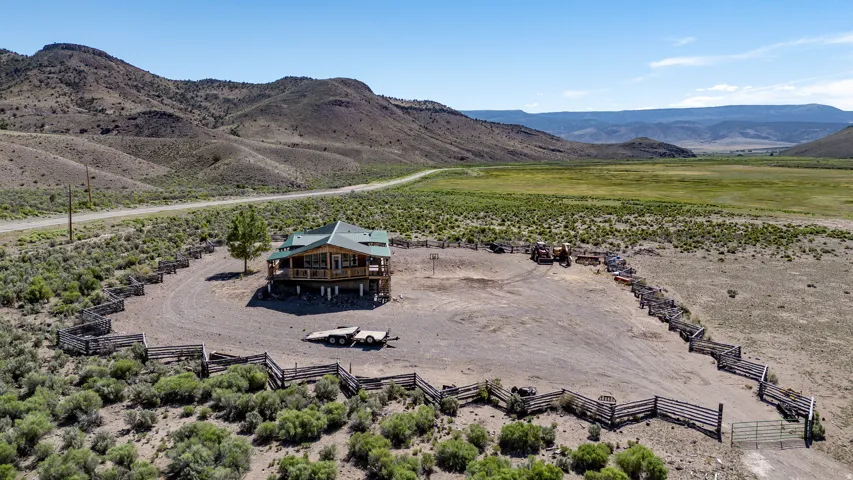 Raised log home with a green roof, featuring a wrap-around porch and a fenced perimeter