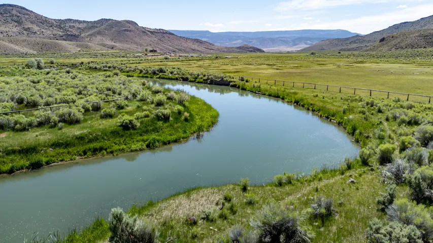 Curving river with lush green banks, bordered by a rustic wooden fence