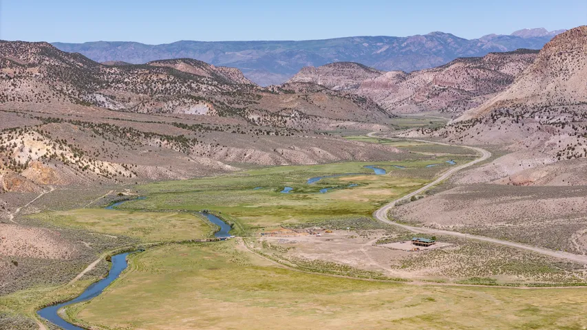Expansive natural landscape featuring a winding river, verdant meadows, and distant mountain ranges