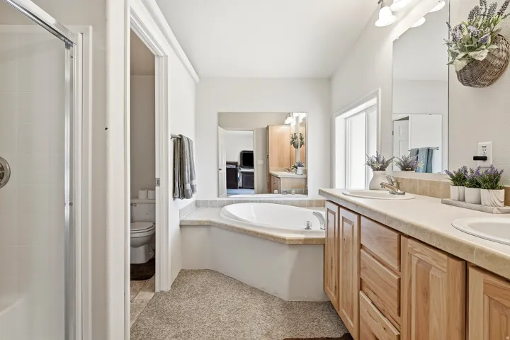 Light-filled bathroom featuring a dual vanity with wood-finish cabinetry, built-in soaking tub, and a separate walk-in shower with glass enclosure