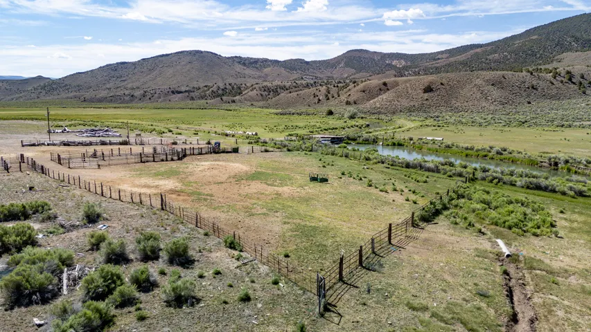 Expansive land featuring a river, multiple fenced areas, and a mountainous backdrop