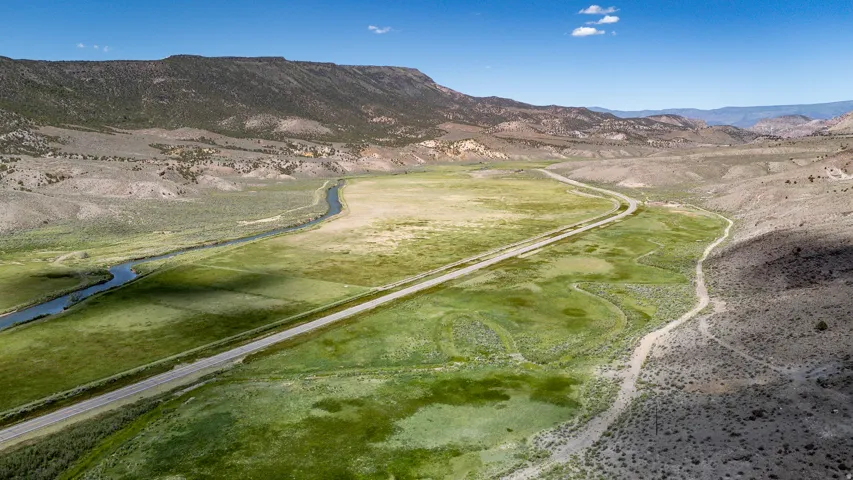 Expansive valley landscape with a winding river, paved road, and distant mountain ranges under a clear sky