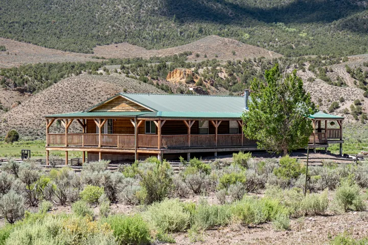 Elevated log cabin style residence featuring a wraparound porch and an extended covered patio