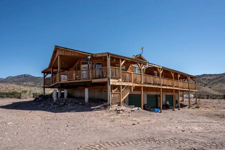 Wood-sided residence featuring a wraparound upper-level deck with wood railings, supported by visible pilings