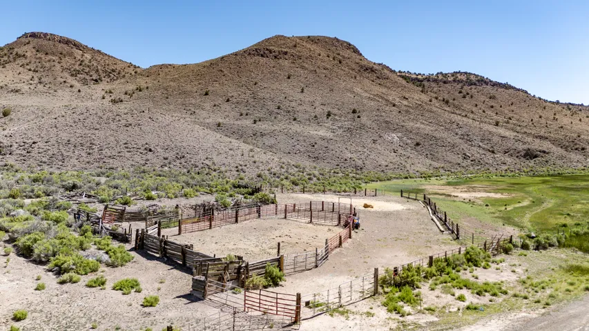 Fenced corral system with various gates, surrounded by arid landscape and distant hills