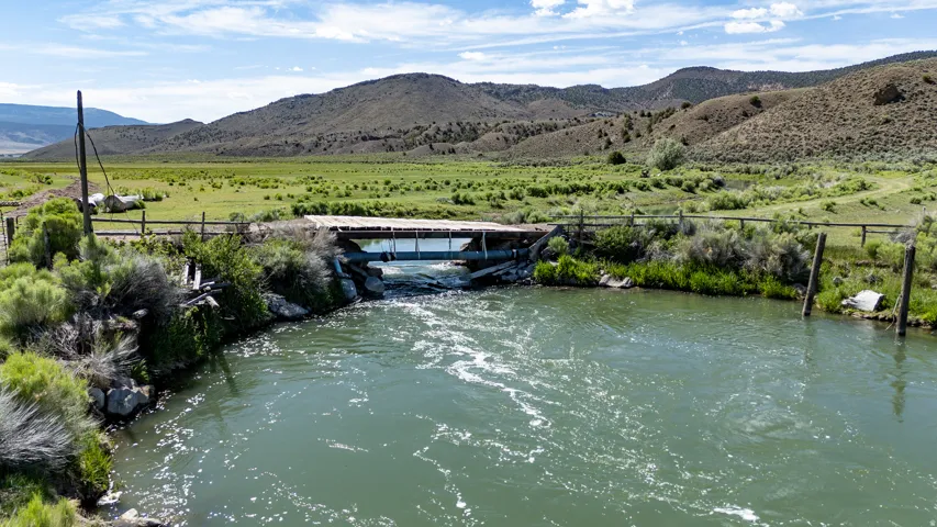 Natural waterway with a rustic bridge and surrounding green landscape