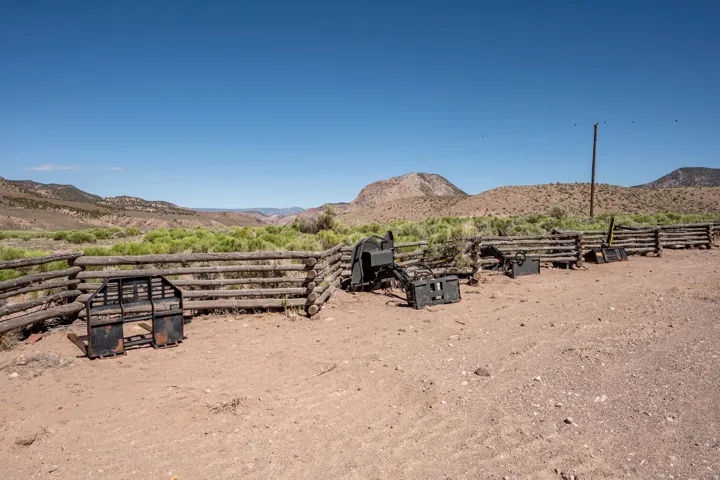 Wooden log fencing defines the property boundary, with a vast, undeveloped landscape featuring distant mountains under a clear sky