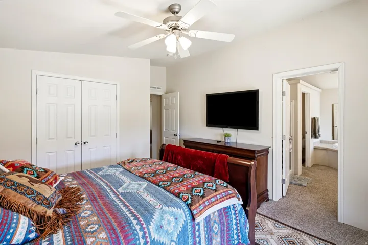Carpeted room featuring a ceiling fan, white bi-fold closet doors, and an entryway to another space with a built-in tub