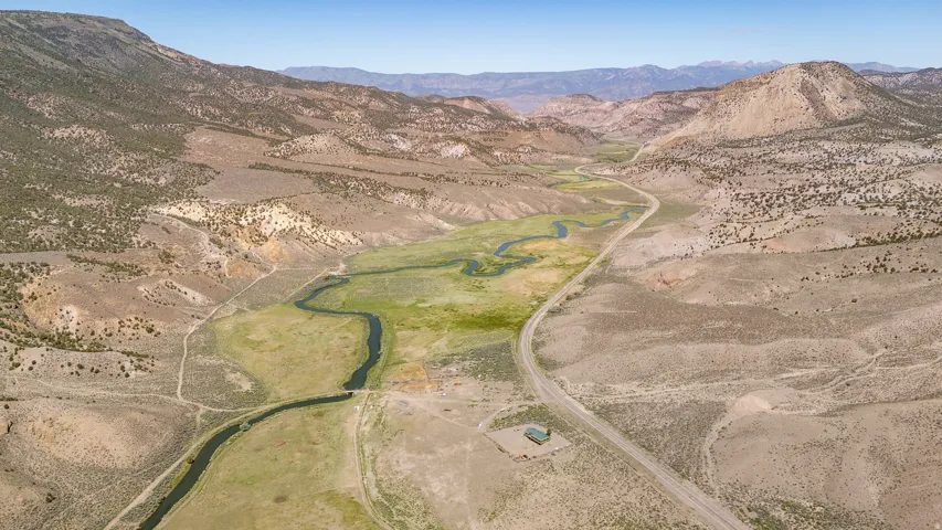 Expansive aerial landscape featuring a winding river, a single-story structure, and a roadway traversing a valley