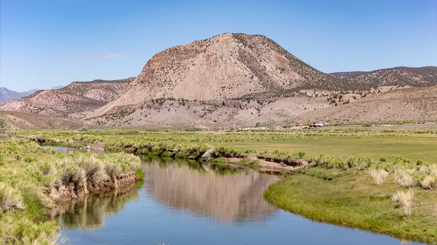 Natural landscape featuring a meandering river and expansive green fields, set against a backdrop of distant mountains