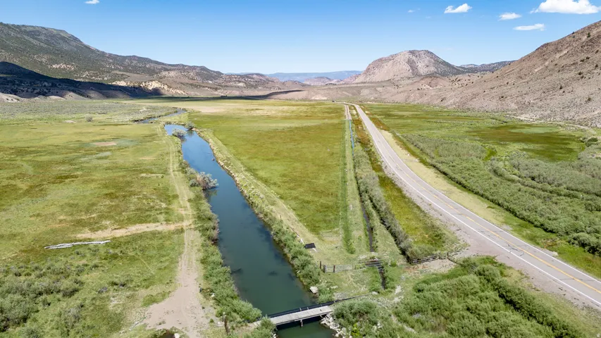 Vast rural landscape featuring a long canal, an expansive grassy field, a paved road, and distant mountains
