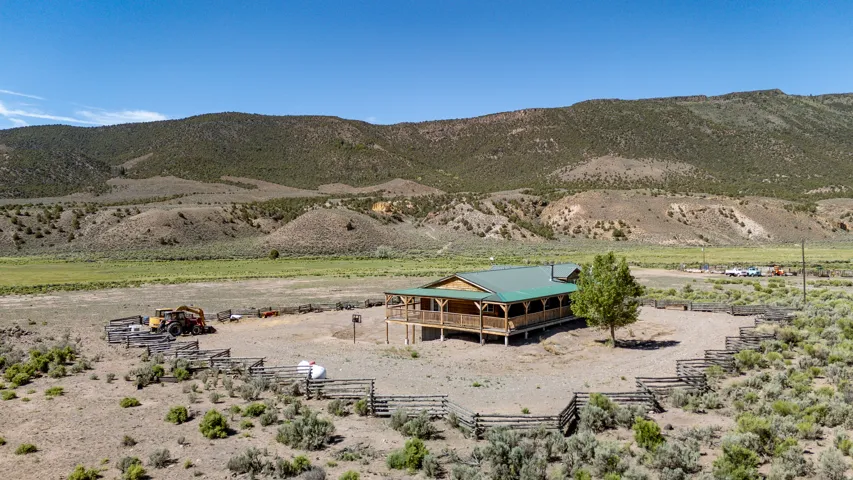 Ranch-style property featuring a green metal roof, a wrap-around porch with wooden railing, and a central fenced area
