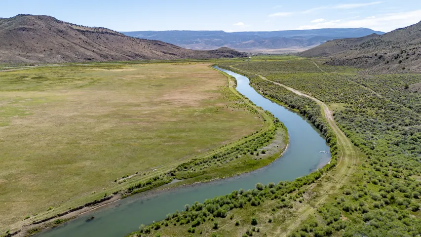 Expansive open land featuring a winding river, distant hills, and clear skies