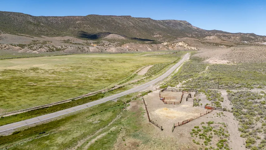 Expansive outdoor landscape featuring a paved road, green pastures, and distant mountains under a clear sky
