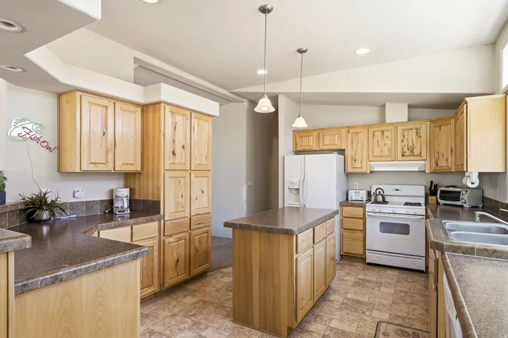 Kitchen featuring light wood cabinetry, a central island with countertop, tile flooring, and integrated white appliances