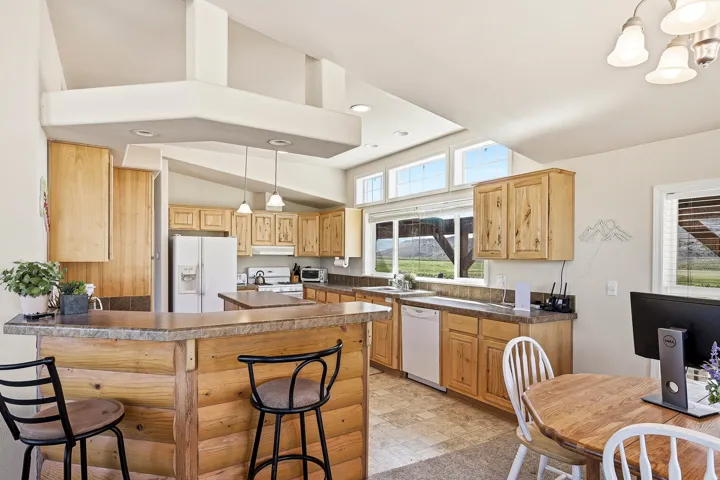 Kitchen featuring wood cabinetry, stone-look countertops, a built-in dishwasher, and vaulted ceilings with recessed lighting