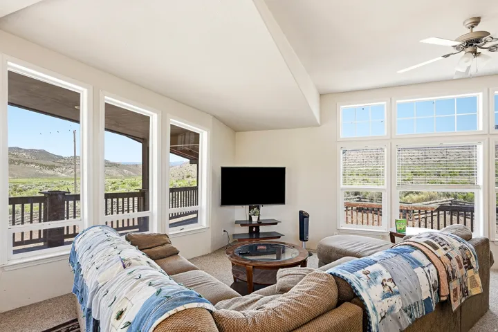 Expansive living area featuring multiple large windows, vaulted ceilings, a ceiling fan, and carpeted flooring