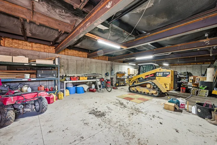 Large utility space featuring concrete flooring, exposed steel beams, concrete block walls, and overhead fluorescent lighting