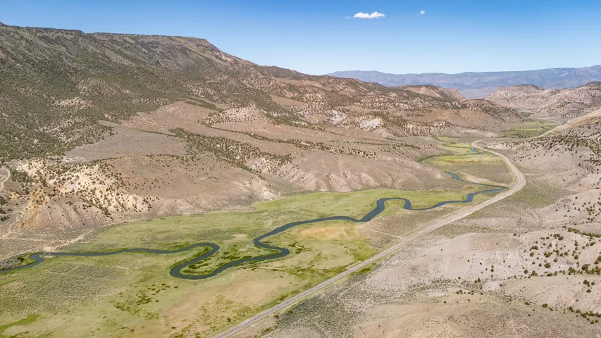 Expansive valley featuring a winding river, verdant riverbanks, surrounding arid hills, and a prominent roadway traversing the landscape