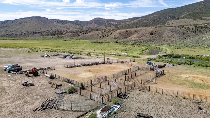 Extensive fenced corrals and pens with a natural water feature and mountainous backdrop