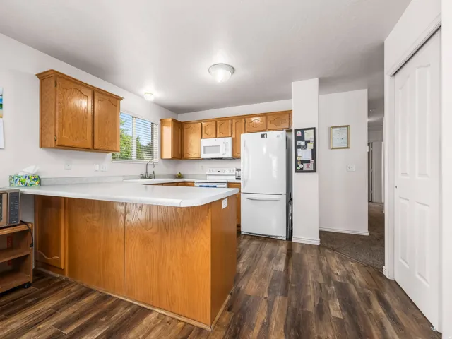 Kitchen featuring wood-finish flooring, wood cabinetry, a breakfast bar, white appliances, and a window with blinds