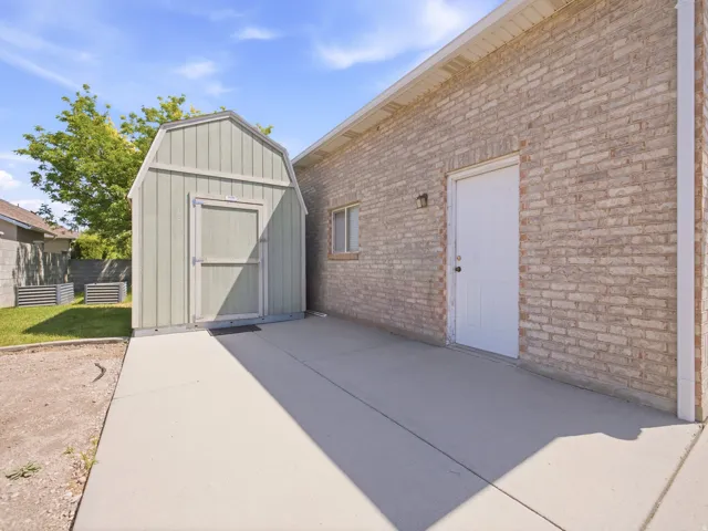 Outdoor storage shed on a concrete slab, complemented by a brick-faced exterior wall with a white utility door and a small window