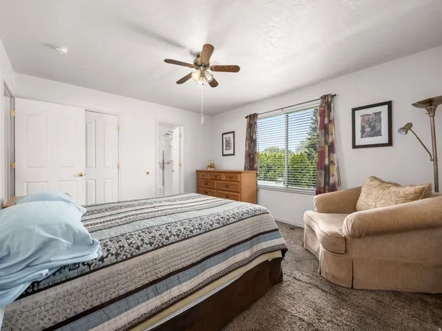 Bedroom featuring a ceiling fan, carpet flooring, and a large window with blinds
