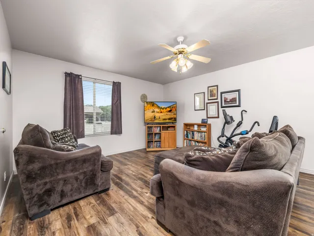 Open concept living space featuring wood-finish flooring, a window with horizontal blinds, and a ceiling fan with integrated lighting