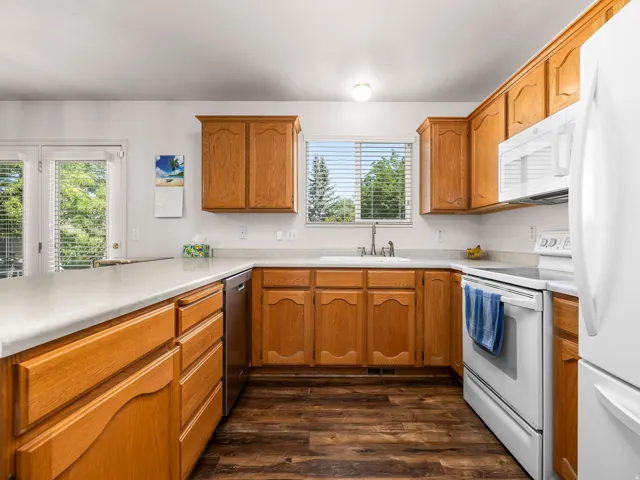 Kitchen featuring wood cabinetry, light-toned countertops, a stainless steel dishwasher, and a white oven/range with an overhead microwave