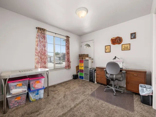 Room featuring carpeted flooring, a window with horizontal blinds, a white entry door with an arched glass insert, built-in shelving, and a flush-mount ceiling light fixture