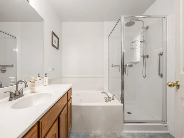 Bathroom featuring a glass-enclosed shower, a built-in jetted tub, a vanity with wood cabinetry, a white countertop, and a single basin sink