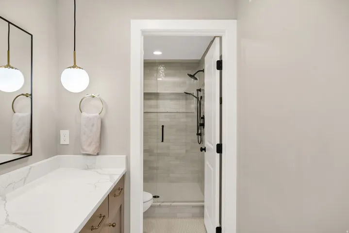 Bathroom vanity featuring a white countertop with grey veining, wood-finish cabinetry, and brass hardware