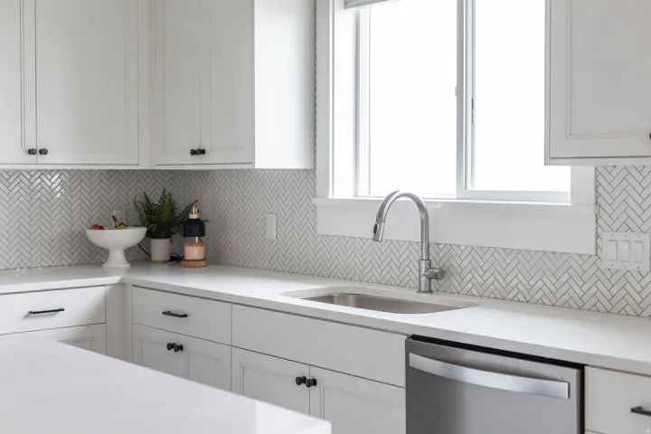 White shaker cabinetry with dark hardware, a stainless steel sink, a pull-down faucet, and a subway tile backsplash in a herringbone pattern
