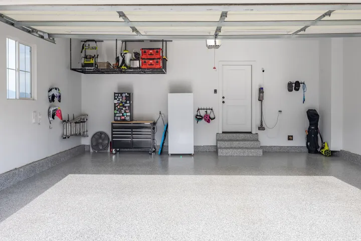 Spacious garage featuring an epoxy-coated concrete floor, overhead storage racking, and a built-in workbench